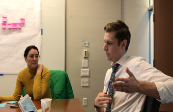 Two participants talking through the design in front of the sticky-note wall